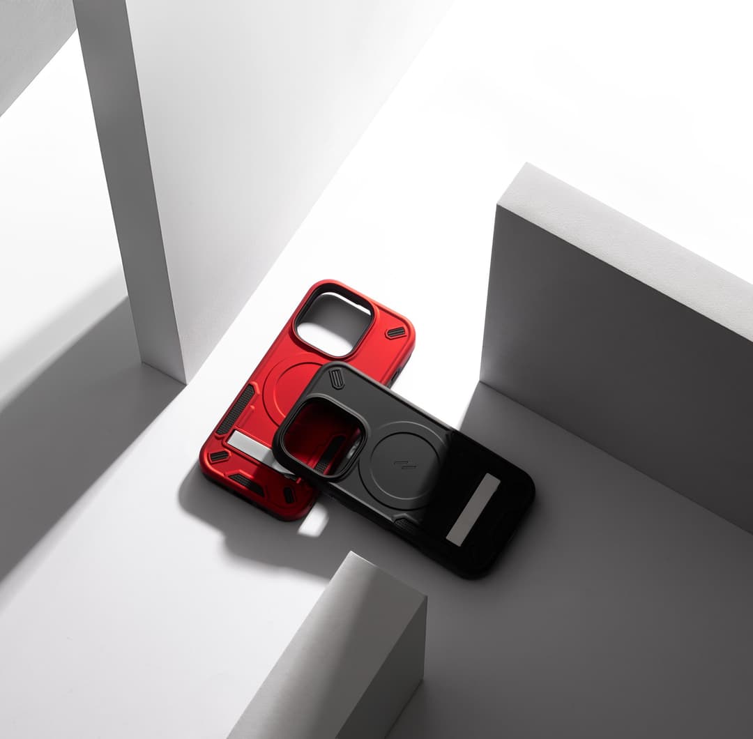 Red and black ZIZO Transform cases leaning together on angular white and gray studio blocks, kickstand tab flipped open and the MagSafe ring visible