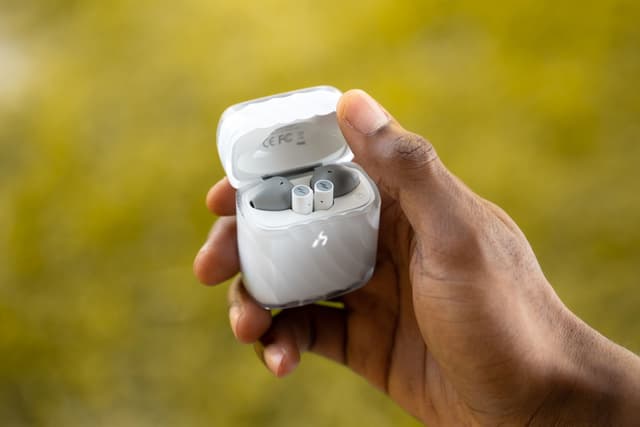A hand holding an open frosted-clear ZIZO Halos charging case outdoors against green foliage