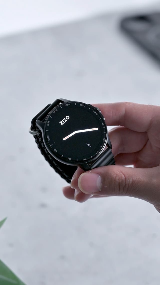 The ZIZO Tyme Elite 2 held in one hand, its round display showing the ZIZO watch face